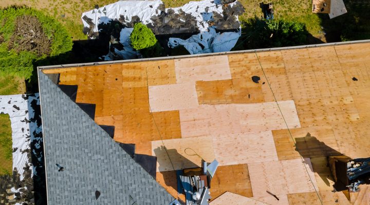 A roofer nailing shingles with air gun, replacing roof cover protection being applied, apartment development